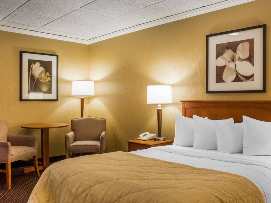 A hotel room with a large bed, two chairs, a small table, and two lamps.