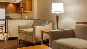 A hotel room with a kitchenette, two armchairs, a wooden table, and a floor lamp. - Clarion Hotel & Suites Riverfront (Oswego)