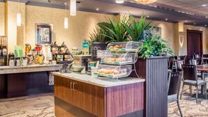 A hotel reception area with a counter displaying breakfast items, a coffee station, and a seating area with tables and chairs. - Clarion Hotel & Suites Riverfront (Oswego)