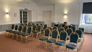 A conference room with rows of chairs, a black table with a nameplate, and a window with a view.