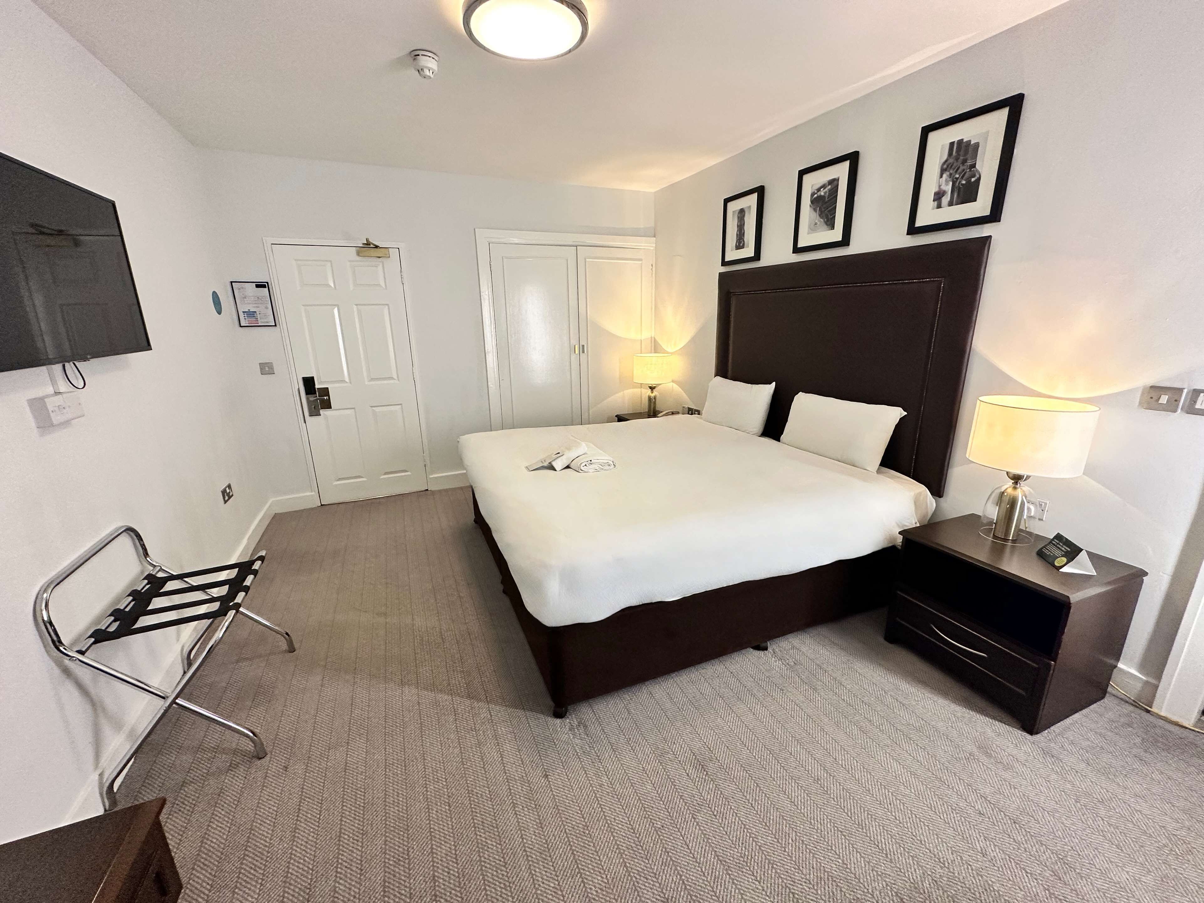A hotel room with a large bed, bedside lamps, a TV, and a chair.