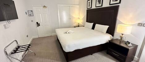 A hotel room with a large bed, bedside lamps, a TV, and a chair.
