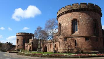 A historic building with two round towers and arched windows, surrounded by a landscaped garden with flowers and benches.