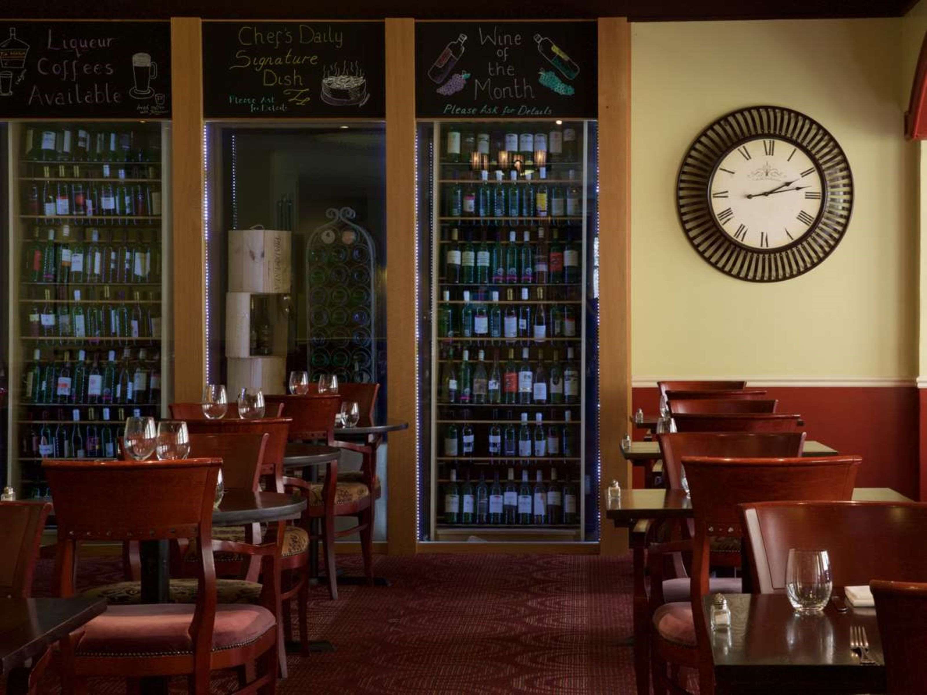 A bar area with wooden chairs and tables, shelves of liquor bottles, and a wall clock.