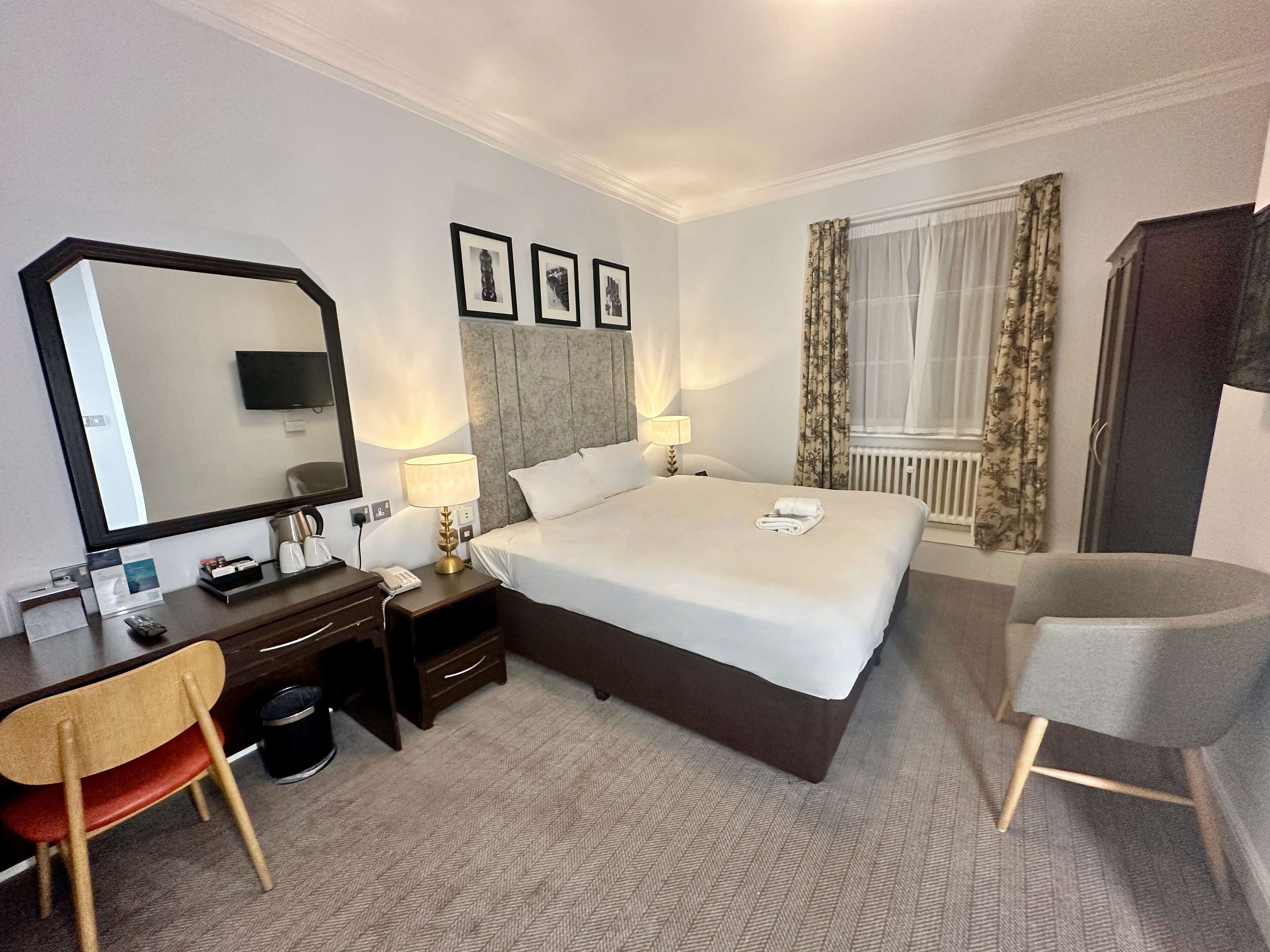 A hotel room with a large bed, a desk with a chair, a mirror, and a television.