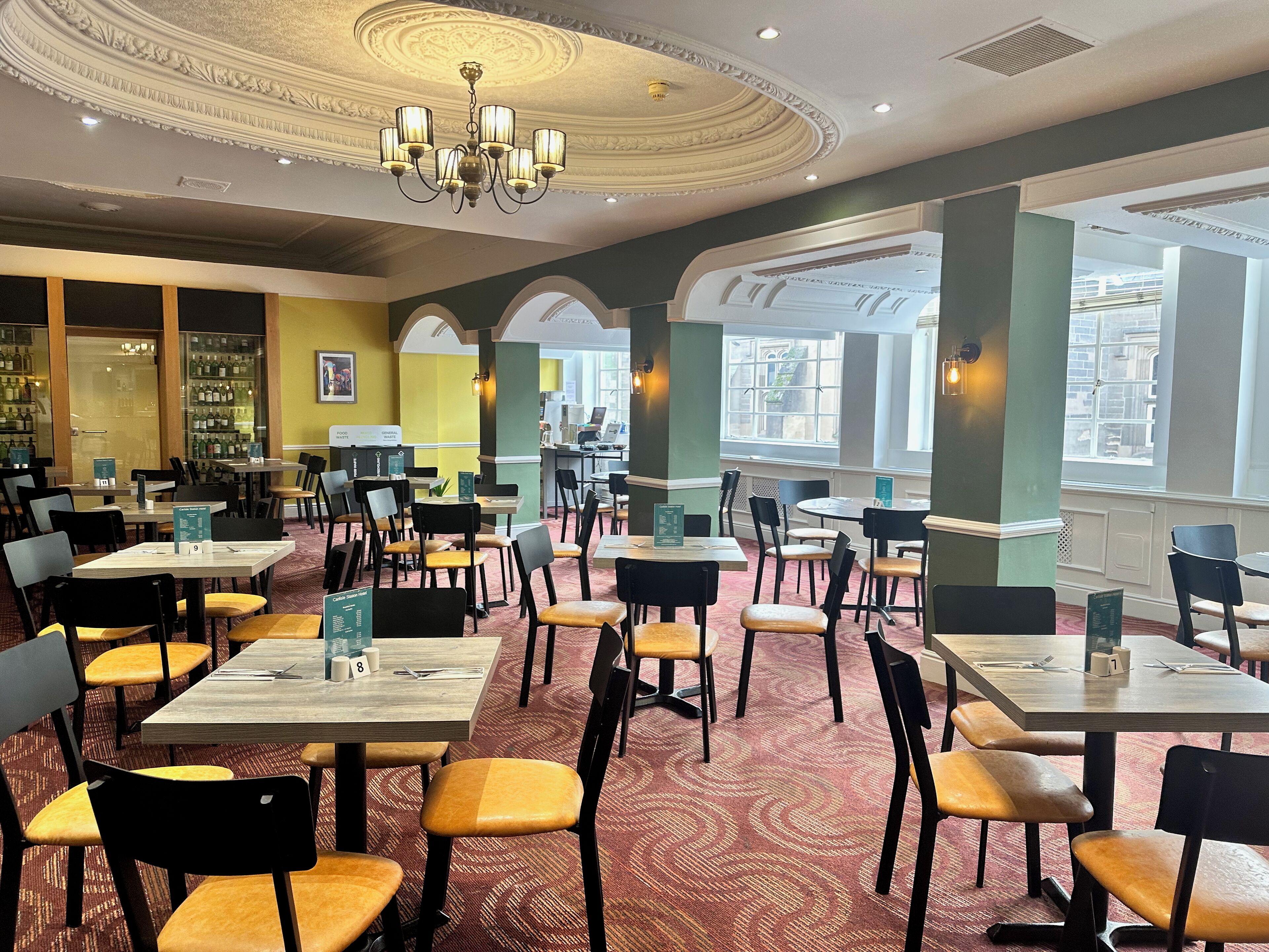 A restaurant with multiple tables and chairs, a chandelier, and large windows.
