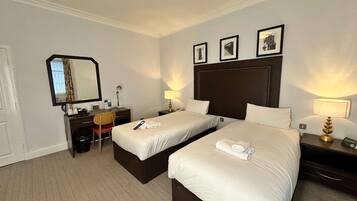 Habitación de hotel con dos camas, un escritorio, una silla, un espejo y lámparas de noche.