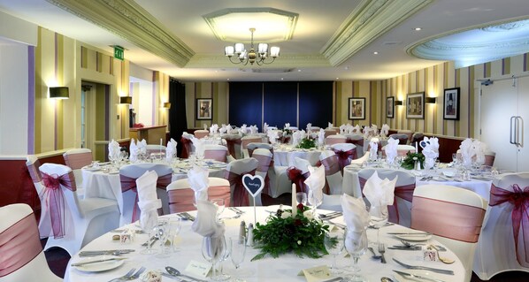 A banquet hall with round tables, white tablecloths, and chairs with pink sashes.