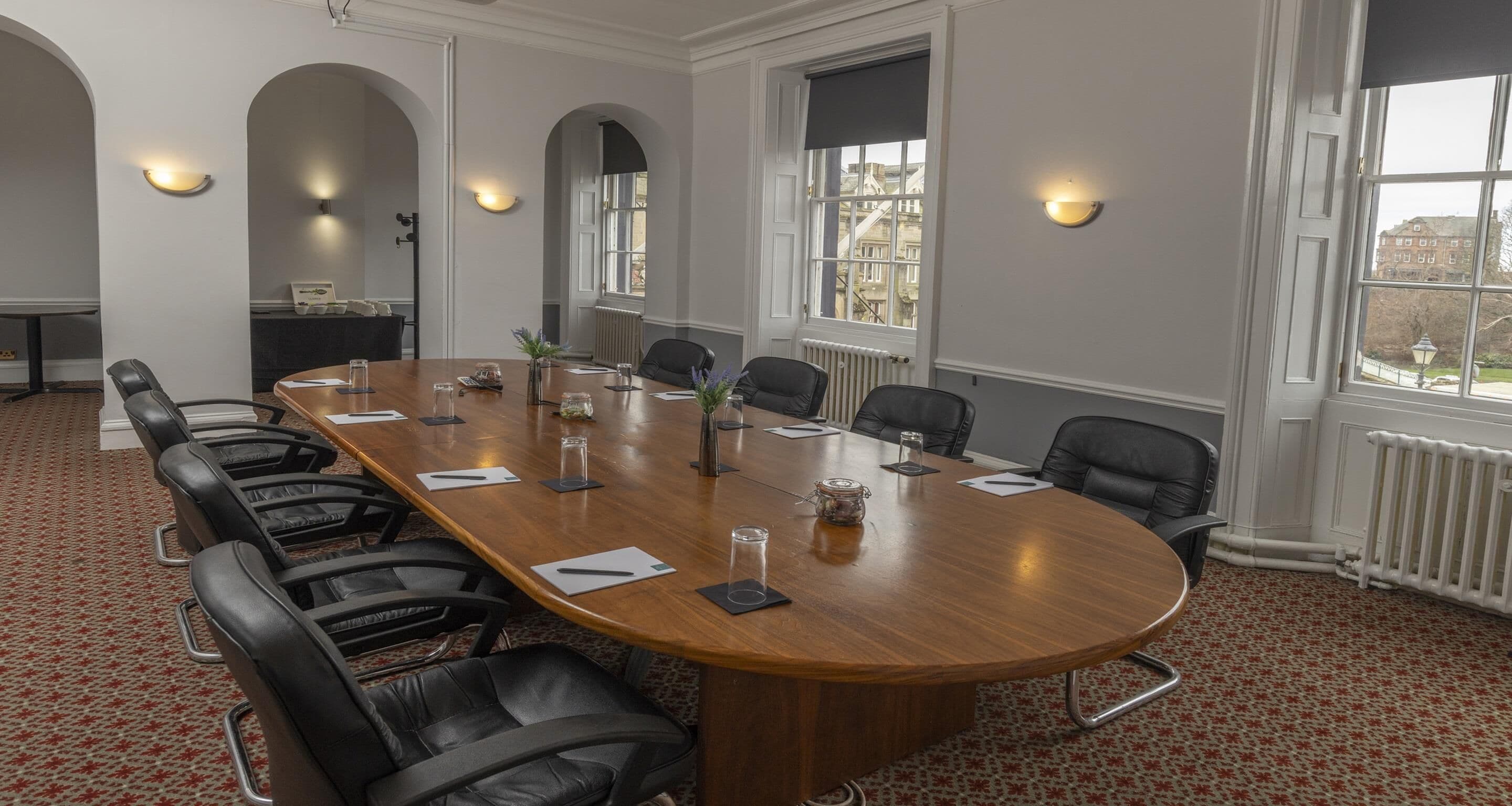 A conference room with a long wooden table, black leather chairs, and a patterned carpet.