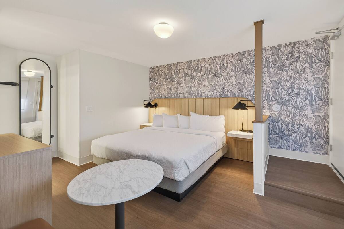 A bedroom with a bed, bedside tables, a nightstand, a mirror, a round table, and a patterned wallpaper.