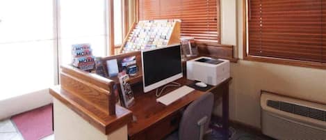 A small office with a wooden desk, a computer, a printer, and a window with blinds.