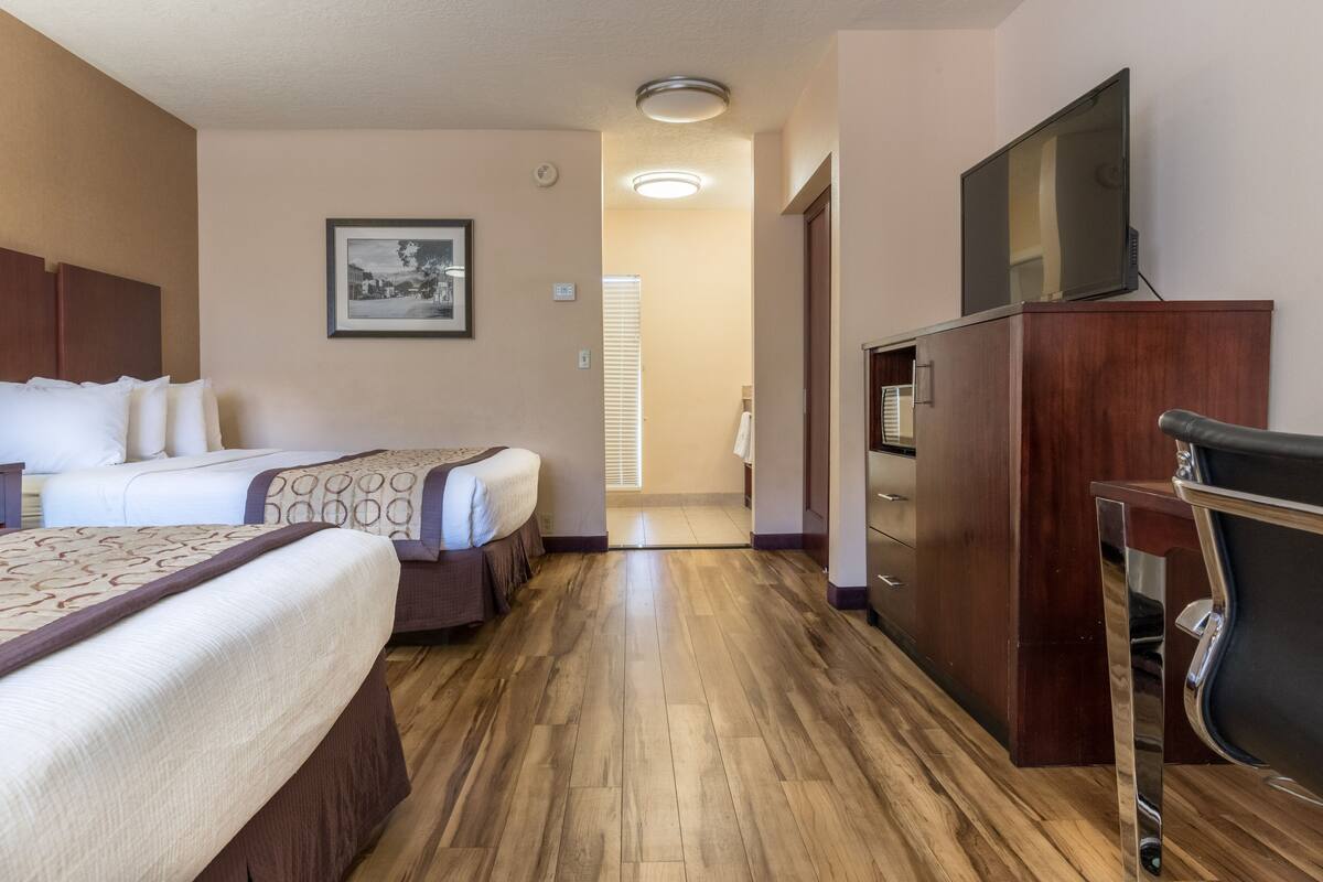 A hotel room with two beds, a wooden floor, a TV, and a desk.