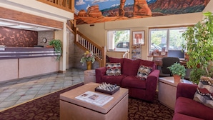 A lobby with a reception desk, a staircase, a red couch, a desk with a computer, and a mural of a desert landscape.