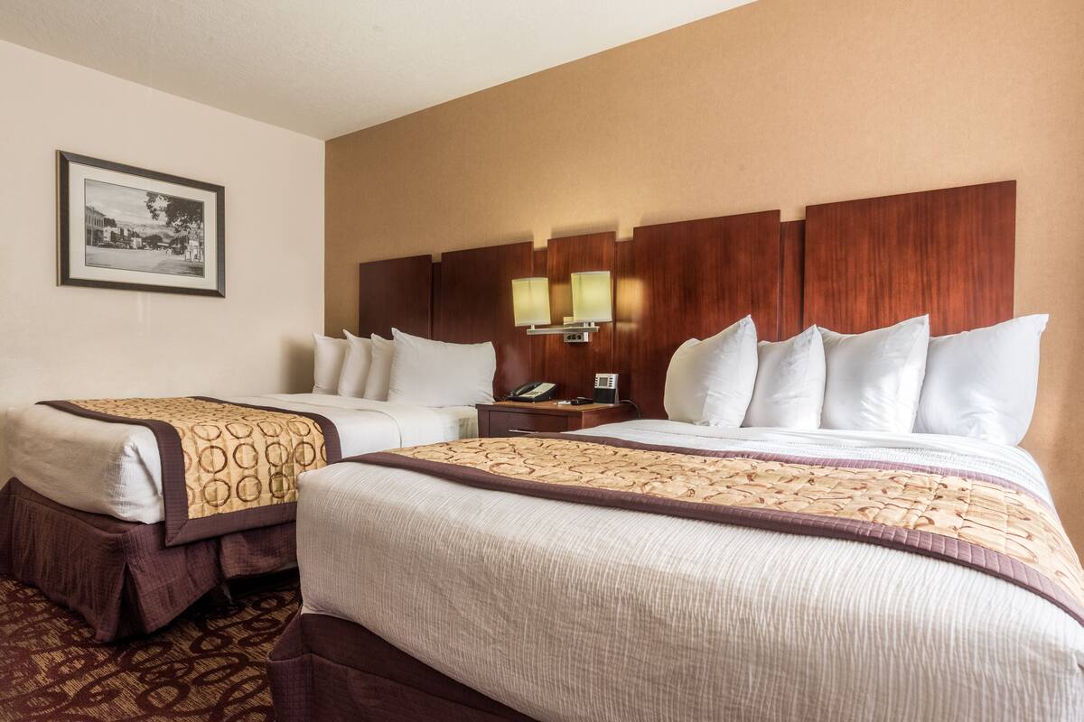 A hotel room with two beds, a nightstand with a phone, and a framed picture on the wall.