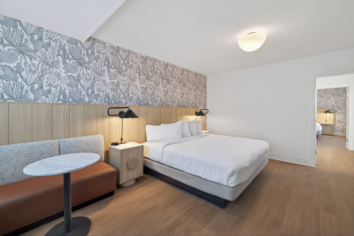A modern hotel room with a bed, a round table, a bench, and a nightstand with lamps.
