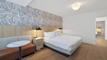 Una habitació d'hotel moderna amb un llit, una taula rodona, una panxa i una petita taula de nit amb làmpades.