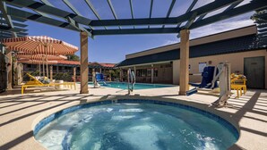 A pool area with a hot tub, lounge chairs, and umbrellas.