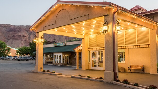 A hotel with a covered entrance, outdoor seating, and a mountain backdrop.