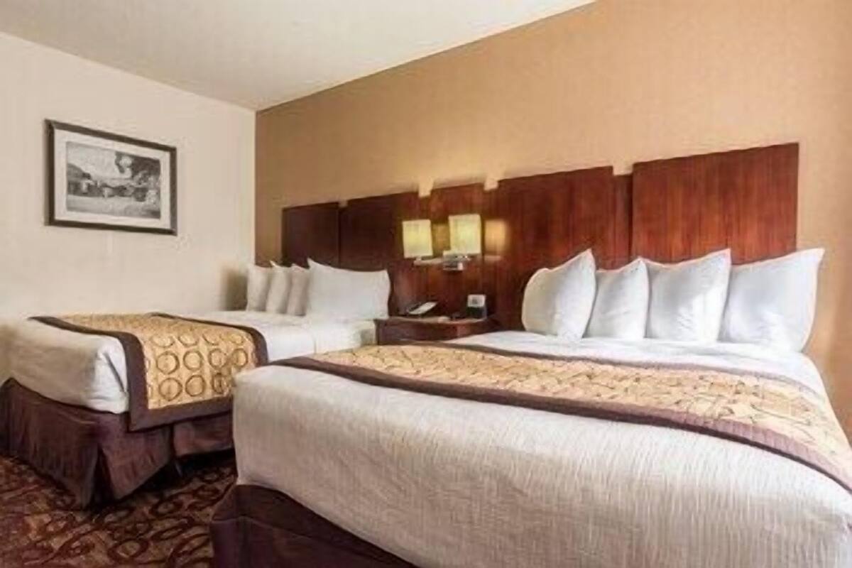 A hotel room with two beds, a wooden headboard, a nightstand with a lamp, and a framed picture on the wall.