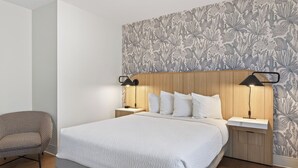 A modern hotel room with a large bed, two bedside tables, a chair, and a floral-patterned wallpaper.