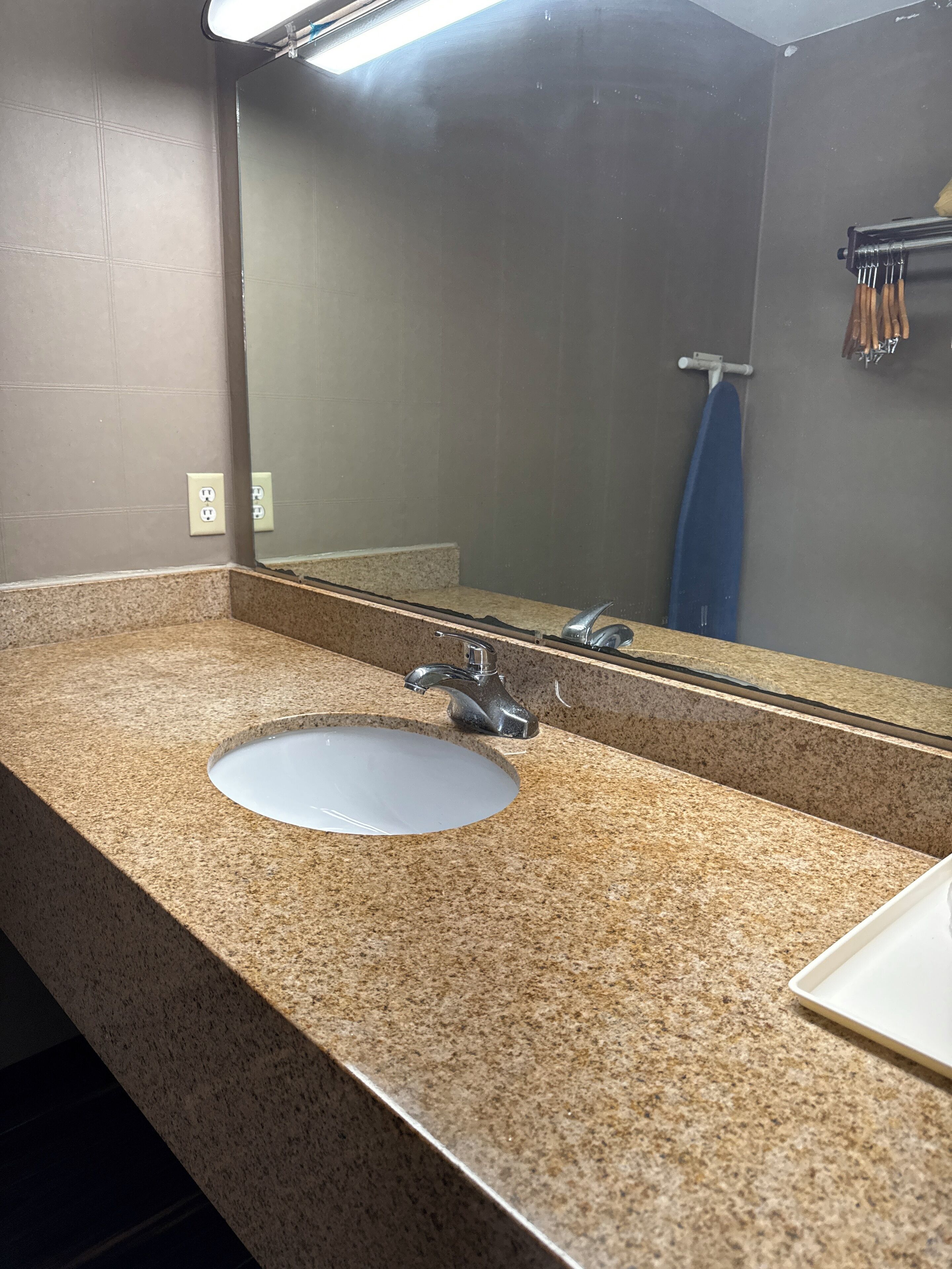 Un baño con encimera de granito, un lavamanos, un espejo y un perchero para toallas.