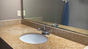 Un baño con encimera de granito, un lavamanos, un espejo y un perchero para toallas.