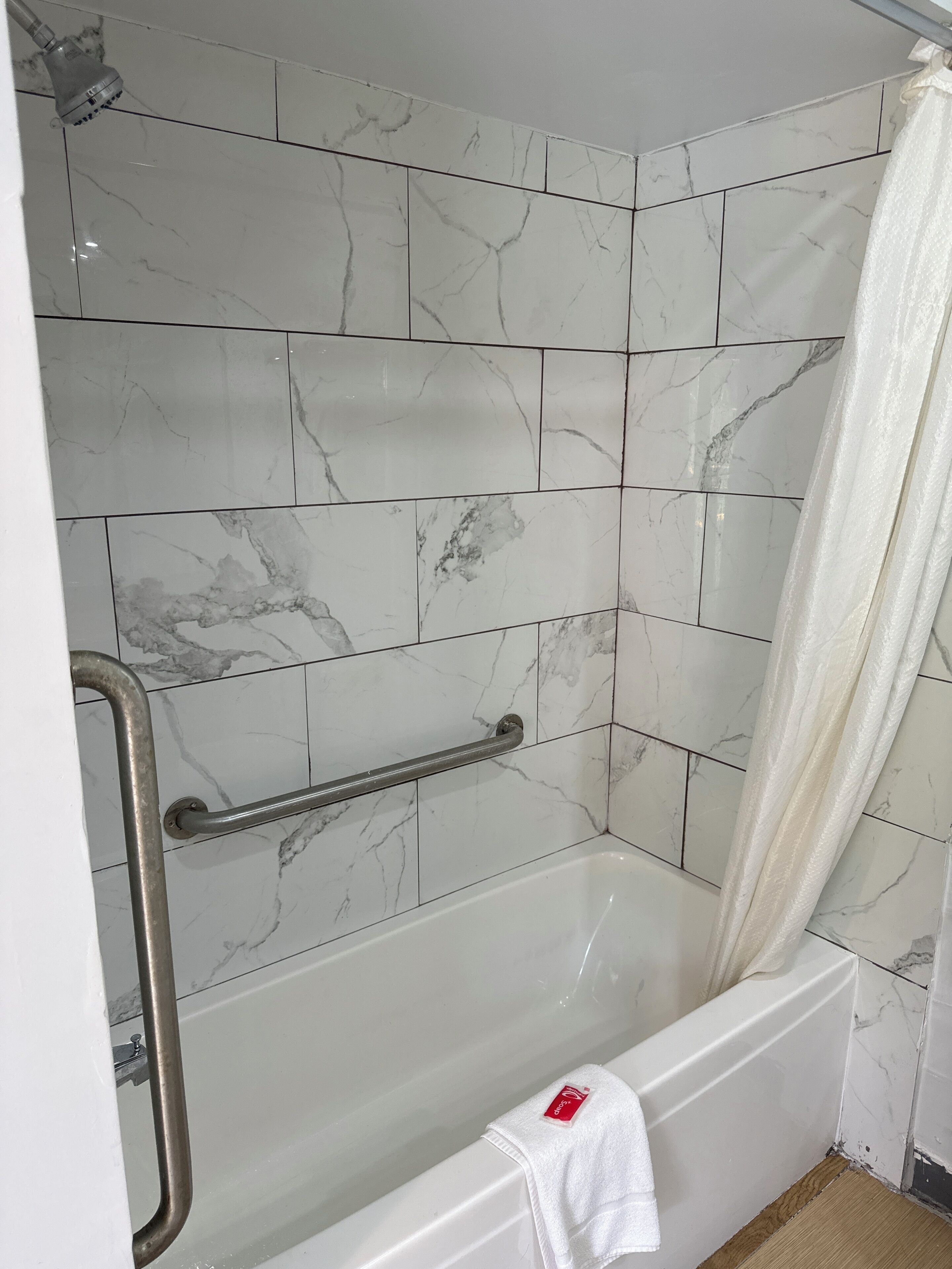 A bathroom with a white bathtub, a shower with a glass door, and a grab bar installed for safety.