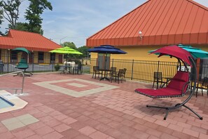 Un área de patio al aire libre con piscina, asientos y sombrillas.