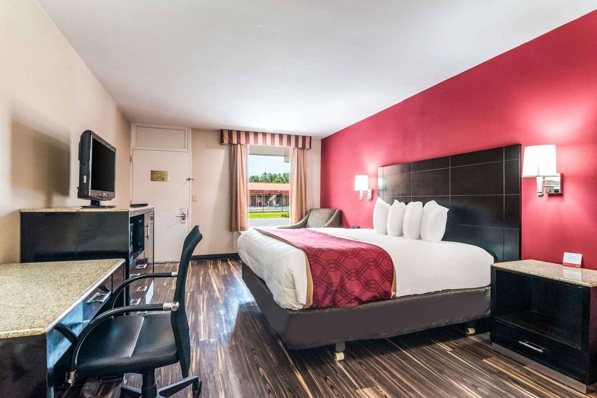 Ein Hotelzimmer mit Bett, Schreibtisch, Stuhl, Fernseher und einem Fenster mit Vorhängen.