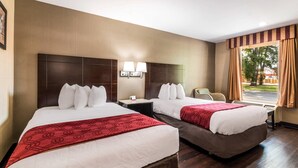 Een hotelkamer met twee bedden, een bureau, een stoel, een raam met gordijnen en een wandlamp.