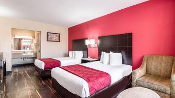 Une chambre d’hôtel avec deux lits, un mur d’accent rouge, une table ronde et une chaise.