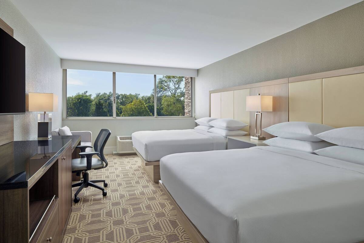 A hotel room with two beds, a desk, a chair, and a TV.