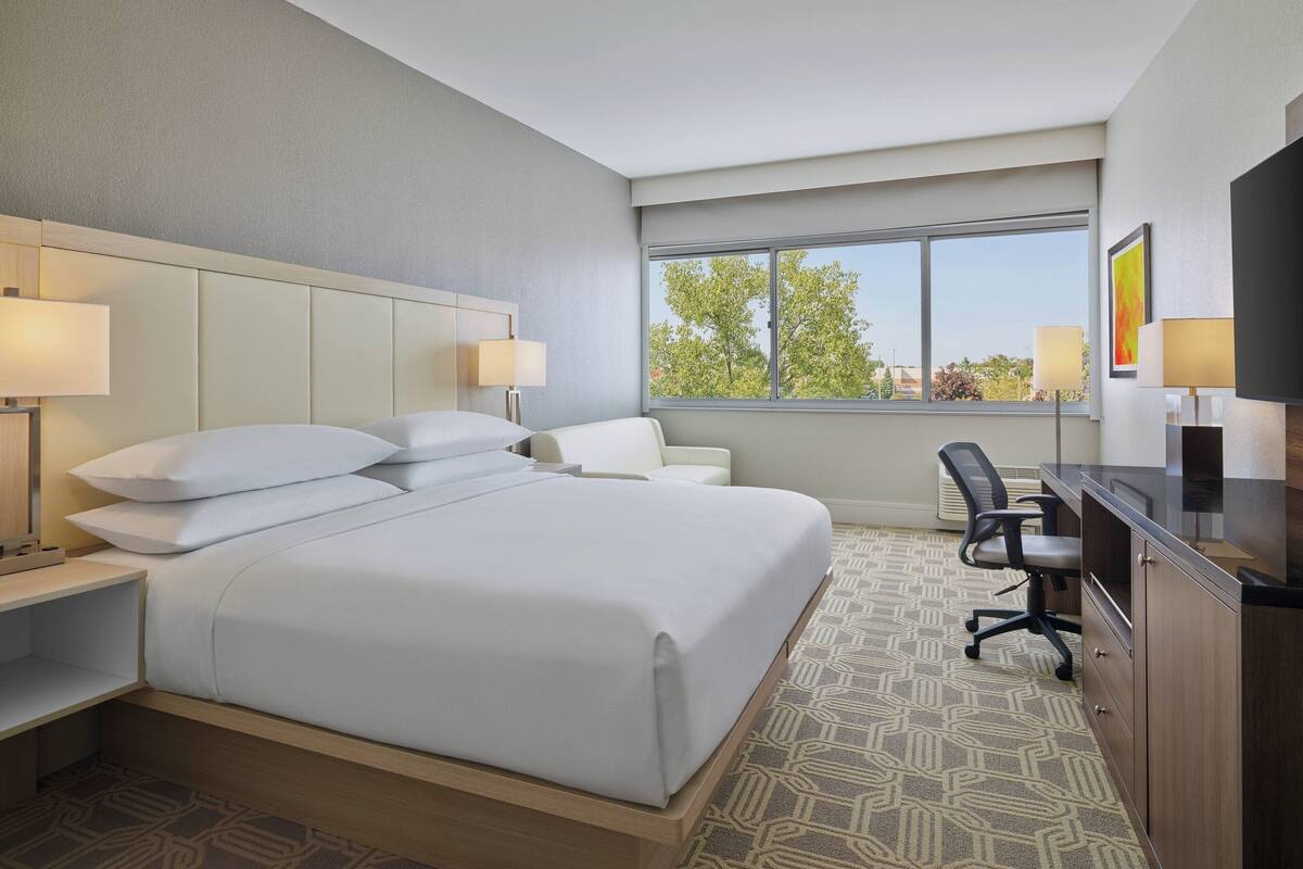 A hotel room with a large bed, a desk, a chair, and a TV.