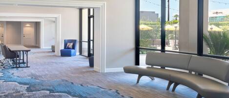 Habitación de hotel moderna con un ventanal grande, un sofá, una mesa de comedor y una silla azul.