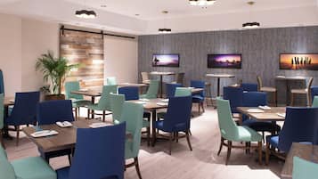 A modern dining area with multiple tables and chairs, a wooden accent wall, and a flat-screen TV mounted on the wall.