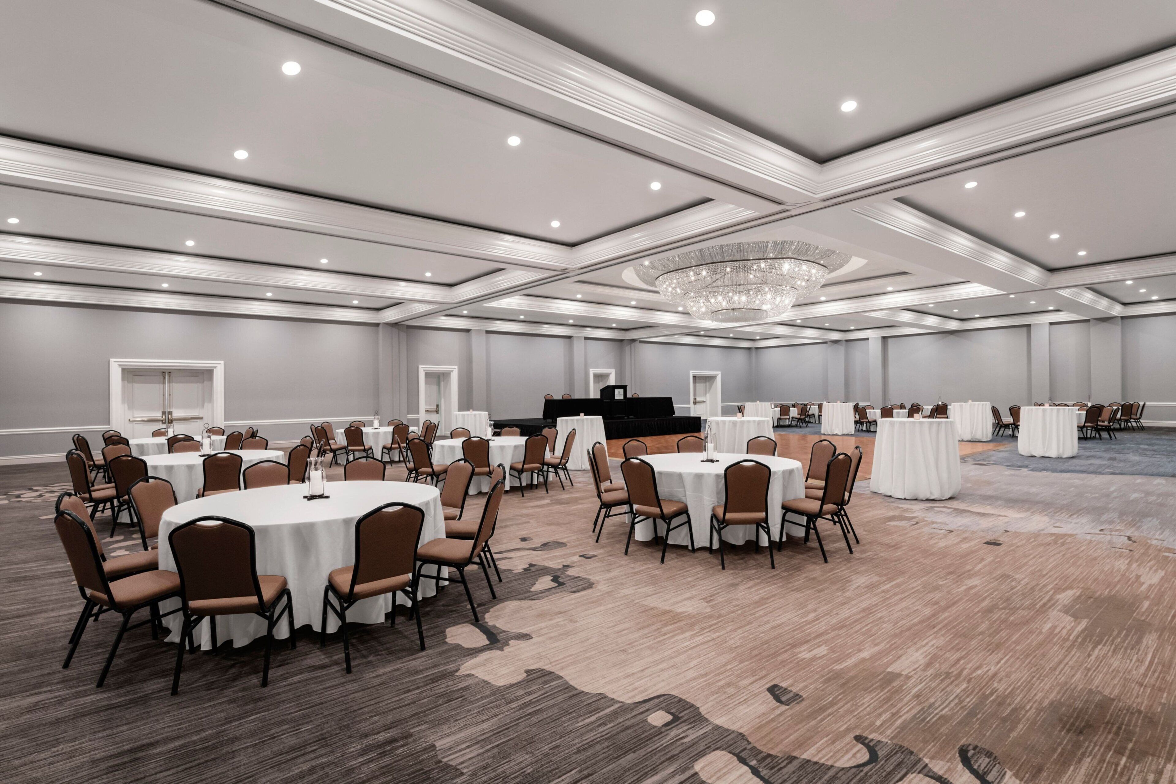 A large conference room with round tables, chairs, and a stage.