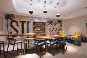 Un comedor moderno con una mesa y sillas de madera, una pared con letras grandes y palmeras, y sillas amarillas.