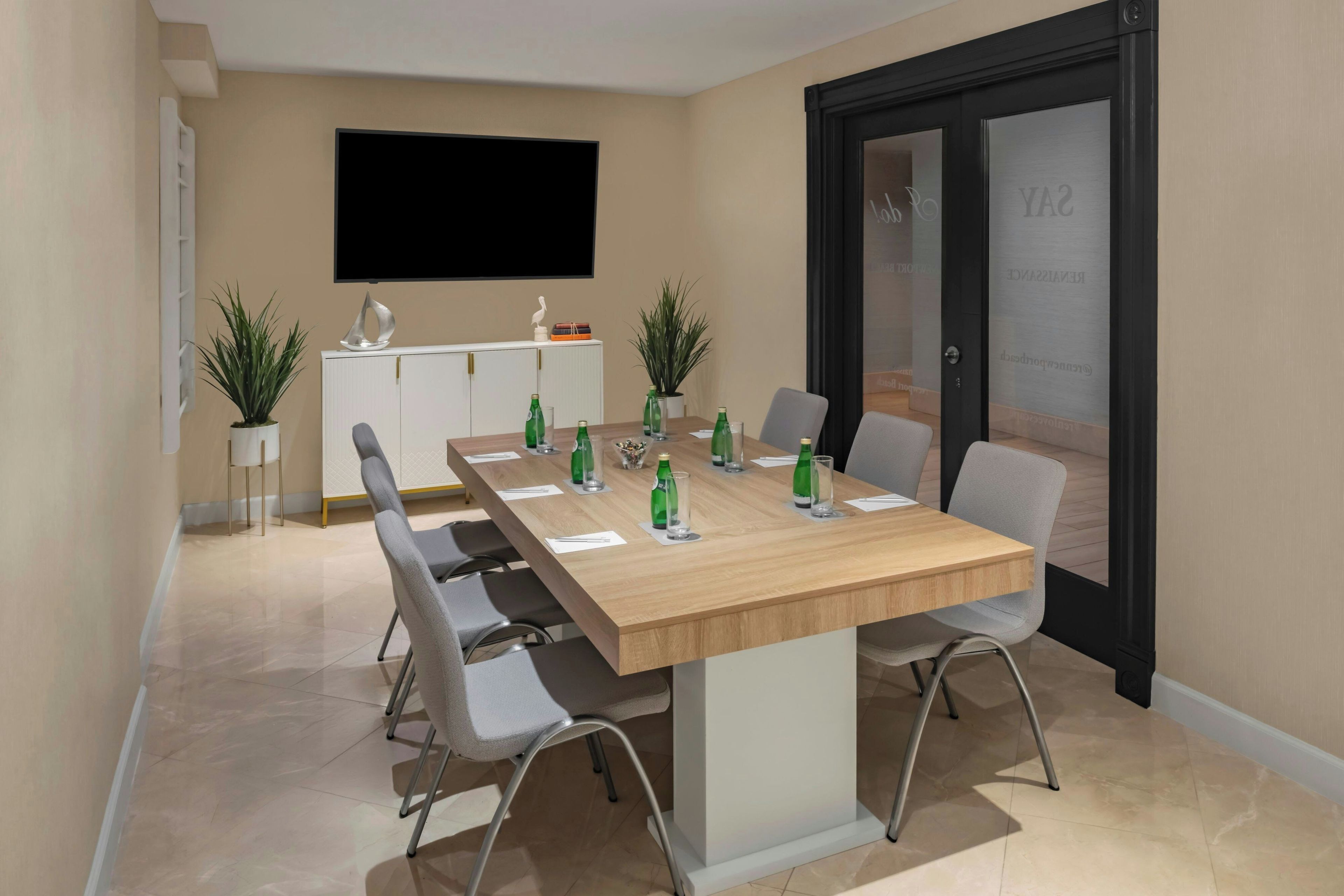A conference room with a long table, chairs, and a television on the wall.