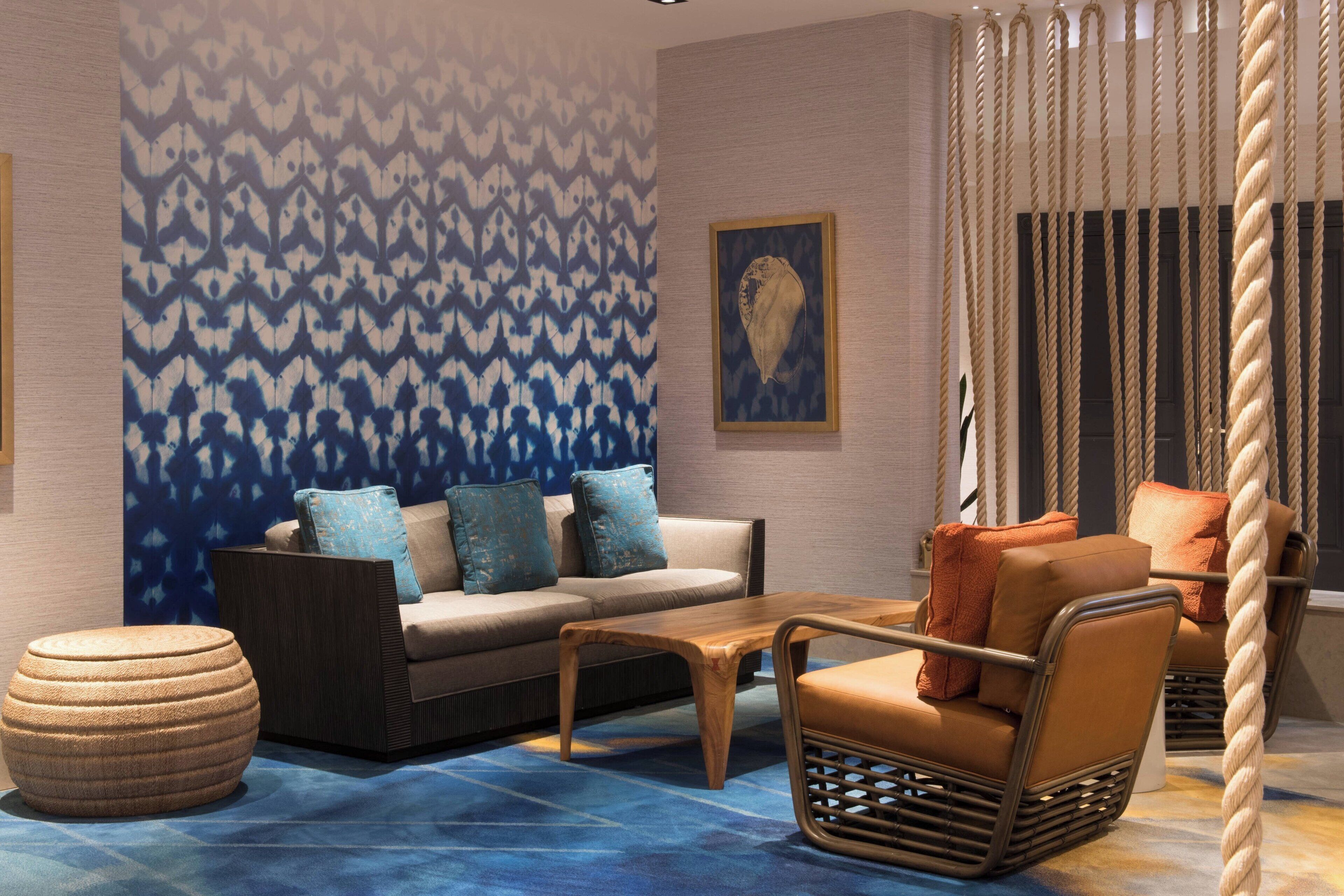 Un espace de détente moderne avec un mur à motifs, un ensemble de canapés, une table basse en bois, un fauteuil en osier et une balançoire en corde.