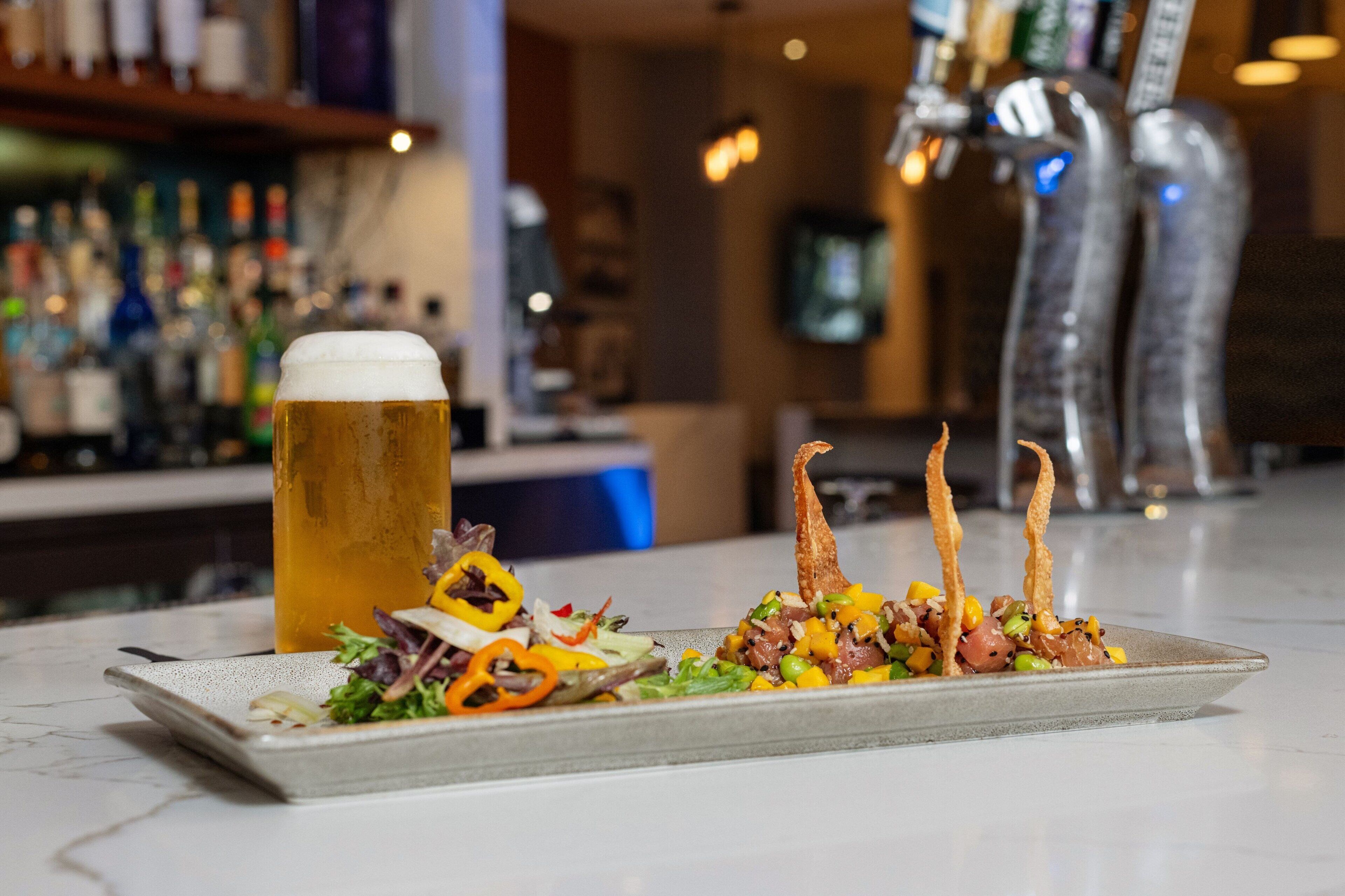 Un bar con cerveza, comida en un plato y una barra.
