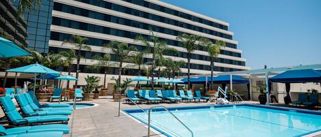 A pool area with lounge chairs and umbrellas, a clear sky, and a modern building in the background.