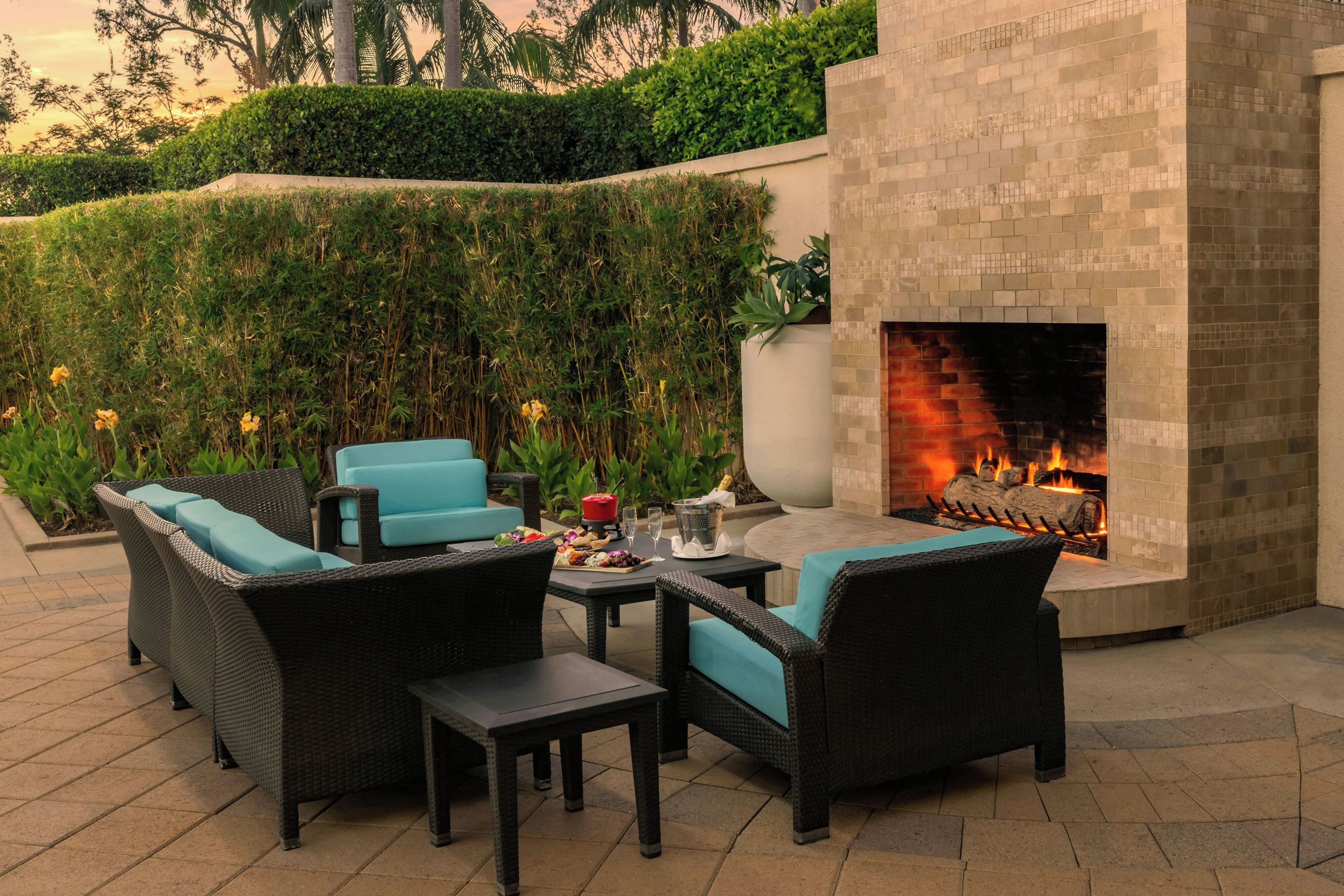 An outdoor patio area with wicker furniture, a table with a spread of food, and a built-in fire feature.