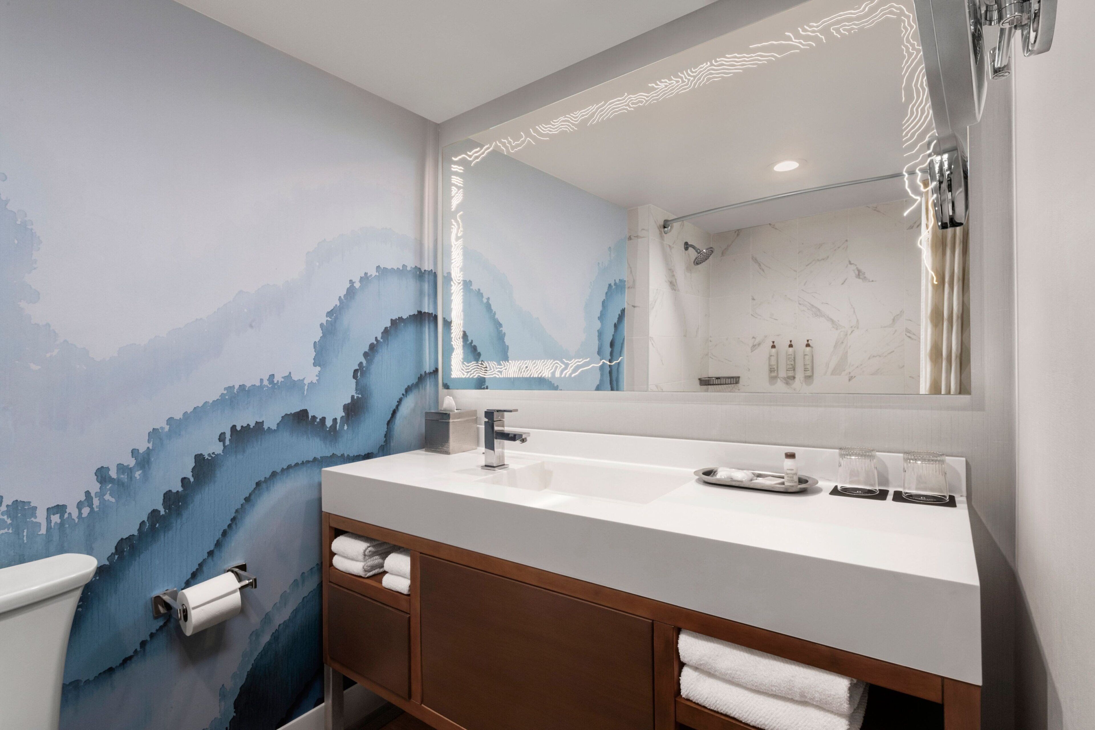 A bathroom with a large mirror, a white sink, and a wooden vanity.