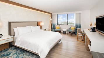 Habitación de hotel con una cama grande, un escritorio con televisor y un espacio de descanso con sillas y una mesita.