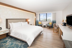 Habitación de hotel con una cama grande, un escritorio con televisor y un espacio de descanso con sillas y una mesita.