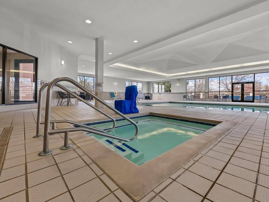 Una piscina interior con suelo de baldosas, una escalera metálica y una zona cubierta con sillas.