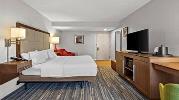 Quarto de hotel com cama, abajures, televisão, escrivaninha e uma cadeira.