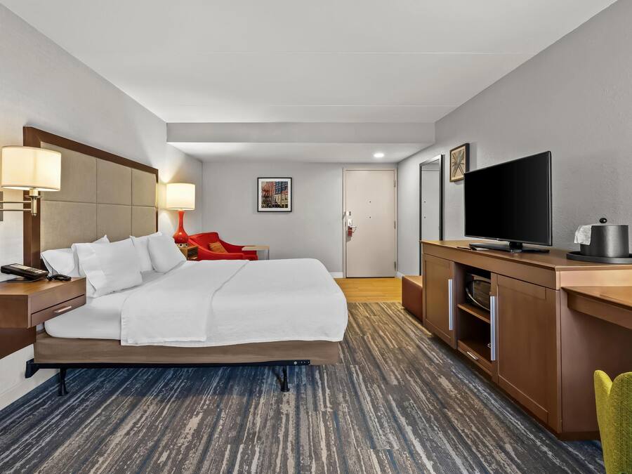 Quarto de hotel com cama, abajures, televisão, escrivaninha e uma cadeira.