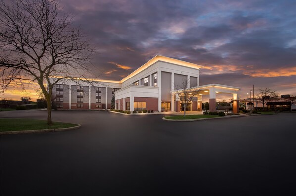 A modern building with a large entrance and a covered area, surrounded by a parking lot and a tree.