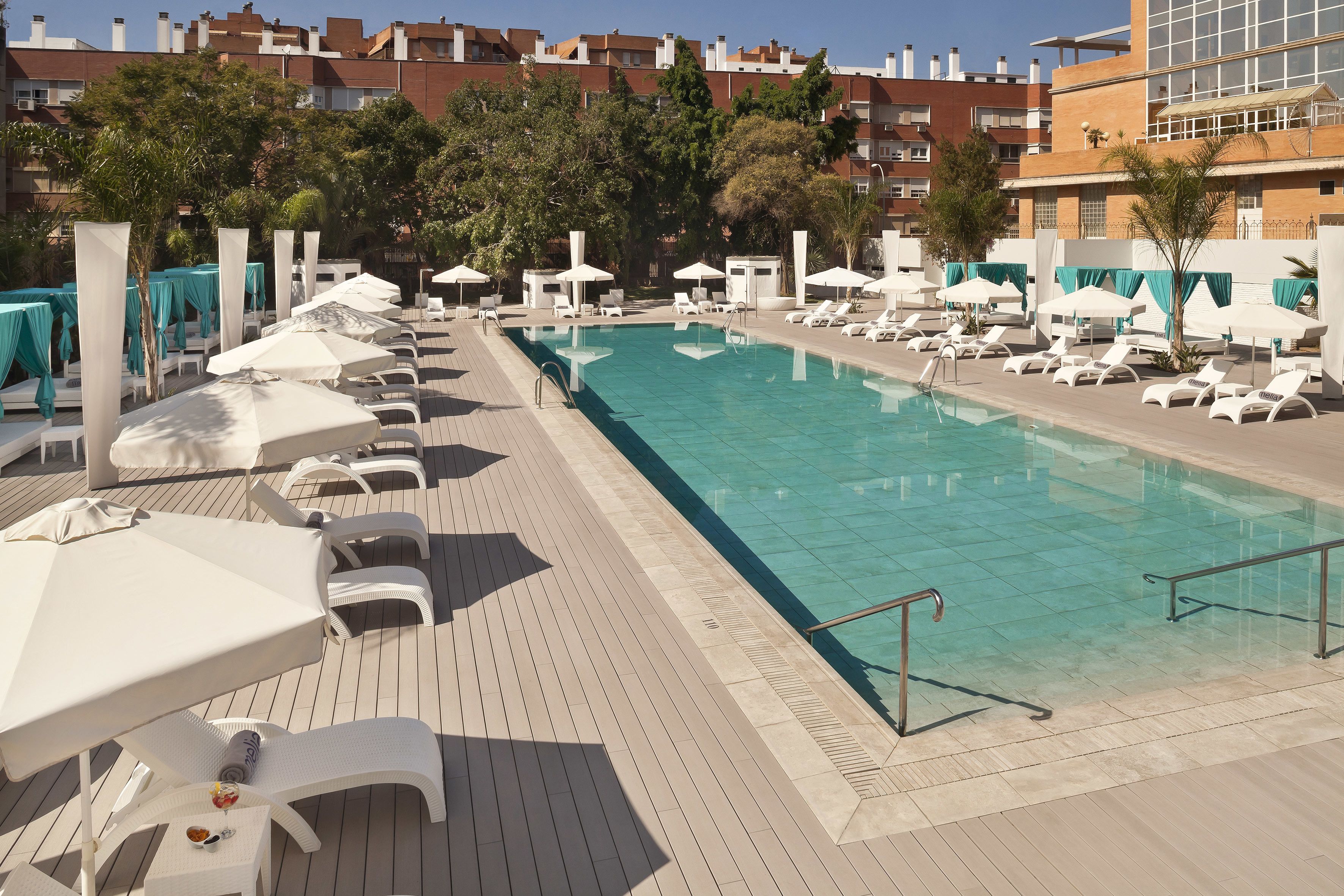 Un espace piscine doté de chaises longues et de parasols, entouré d’immeubles.